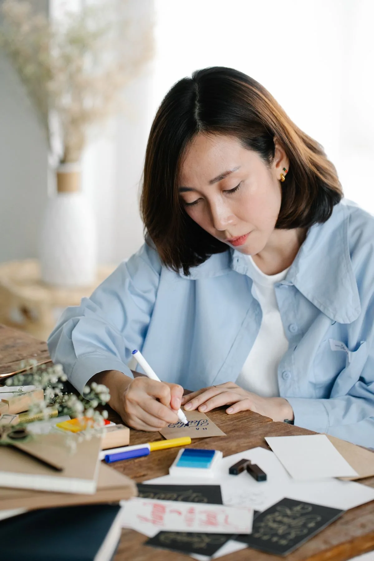 Cô gái ngồi viết thư bên bàn có lọ hoa